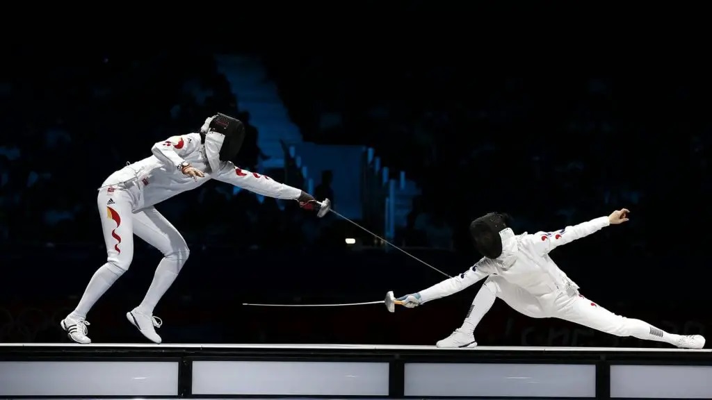 Dos esgrimistas ambos vestidos de blanco con caretas protectoras peleando con espadas en una base