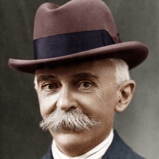 Vista frontal de El Barón de Coubertin con sobrero café y traje gris 