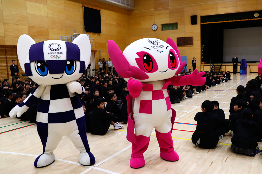 La mascota olímpica de Tokio 2020 de color azul Miraitowa y la mascota paralímpica de color rosa llamada Someity posando en un área con niños