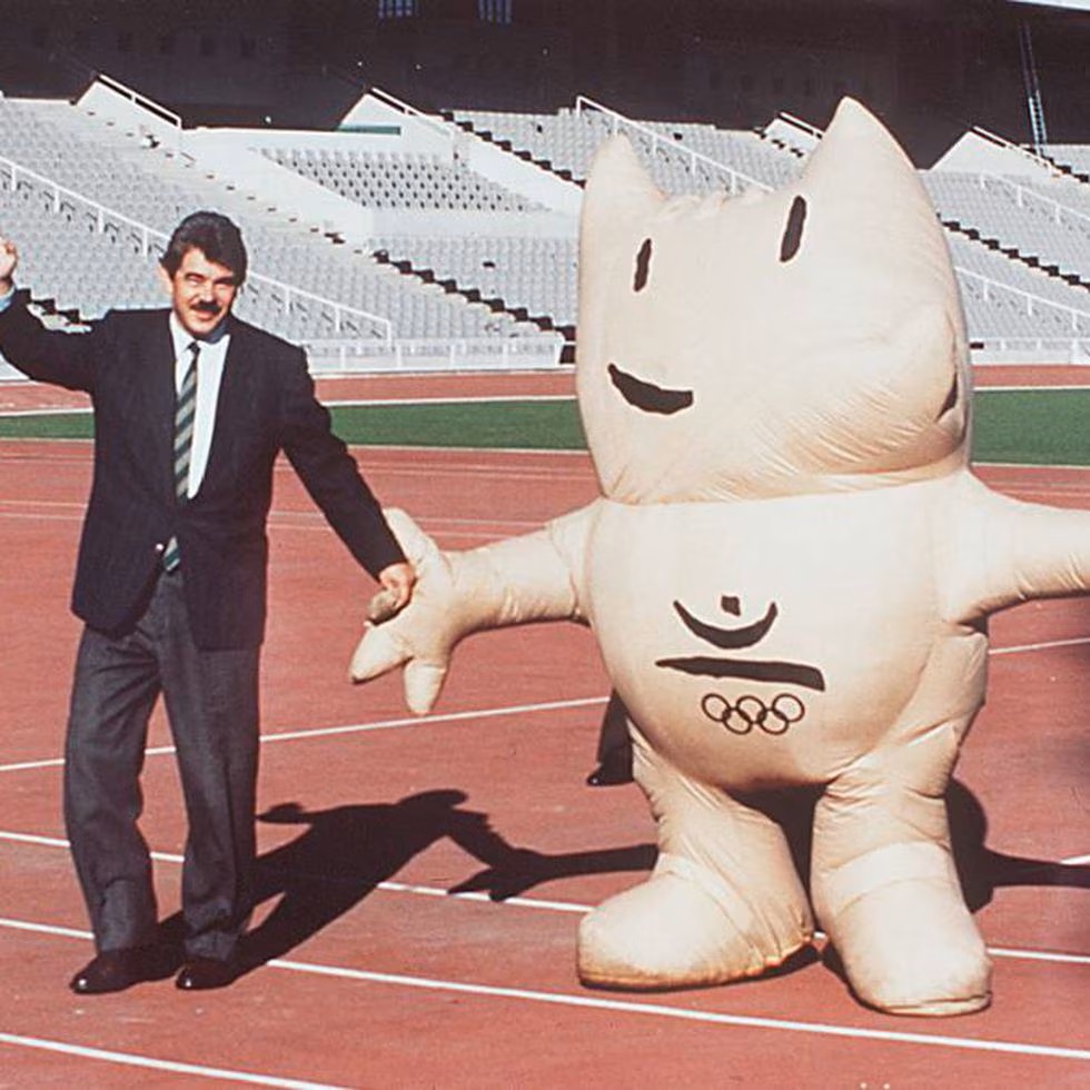 Mascota Cobi de color hueso agarrado de la mano con representante de los juegos Olímpicos en una pista de atletismo